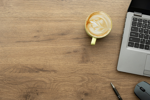 Wood office desk table with laptop computer, cup of latte coffee and office supplies. Top view with copy space, flat lay.