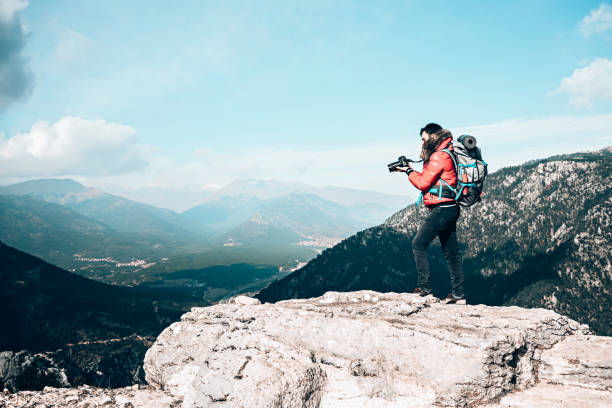 istock Photographer on mountain top taking photos over clouds. 1394913626