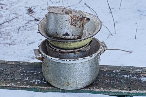 part on a old dirty metal bowls and pans stand on a wooden bench in white snow on a winter street