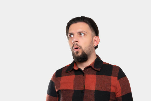 Portrait of a shocked  young man looking away with negative facial expression over gray background Portrait of a young man looking away with shocked facial expression over gray background. Horizontal composition. Studio shot. confusion raised eyebrows human face men stock pictures, royalty-free photos & images