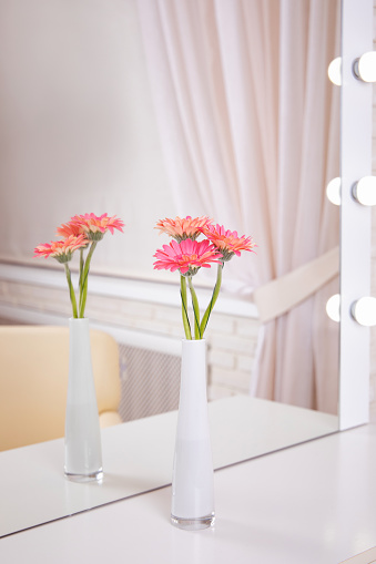Bouquet of beautiful pink gerbera flowers in vase on table near mirror