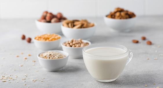 Vegetable milk in a mug on the background of bowls with nuts, oatmeal and legumes. An alternative to dairy products. Healthy lifestyle.