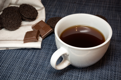 White cup with dark coffee and sweets, close-up