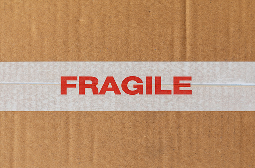 White tape ribbon with the word Fragile in red on cardboard texture