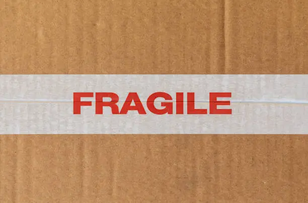 White tape ribbon with the word Fragile in red on cardboard texture