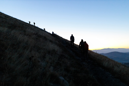 Group of friends hiking on a trail up to the top of Rtanj mountain in Serbia before sunrise, silhouetted against the bright sky