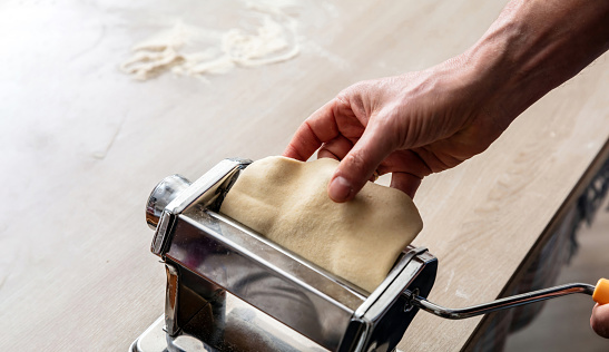 Dough homemade preparation. Fresh pasta maker machine. Male hand making dough phylo for pies and pastry, close up view