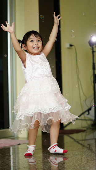 Happy Little girl playing soap bubbles in living room. Joyful kid at home.