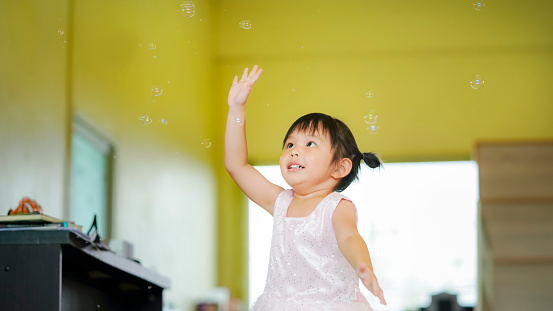 Happy Little girl playing soap bubbles in living room. Joyful kid at home.