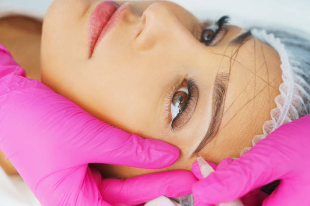 Cosmetologist preparing woman for eyebrow permanent makeup procedure, closeup stock photo