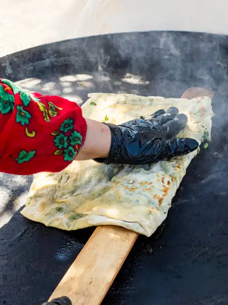 Photo of Village woman baking Turkish pita gozleme with cheese and greens