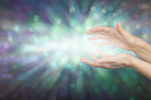 female cupped hands with light between against a green bokeh effect background and space for messages
