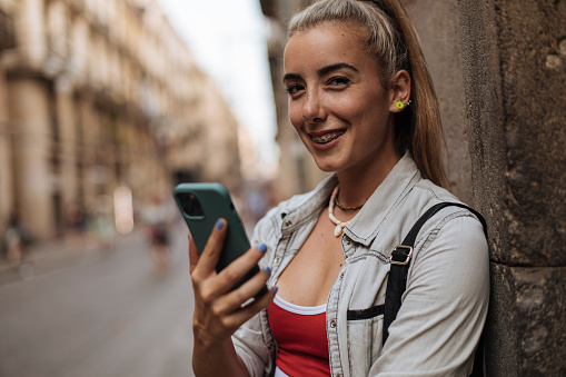 Young female holding smartphone and smiling in the city