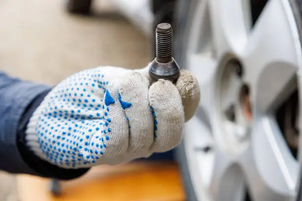 Photo of mechanic hand in fabric glove holding car wheel bolt