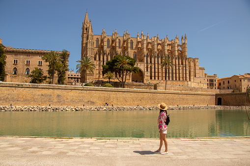 young woman with backpack looking at the imposing cathedral in Palma de Mallorca, Spain