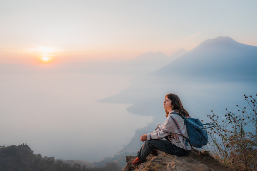 Young Caucasian woman sitting on mountain on  the background of Atitlan Lake in Guatemala at sunset