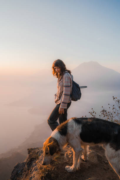 Woman with dog  standing on mountain on  the background of Atitlan Lake in Guatemala at sunset stock photo