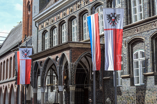 Entrance at the historical town hall of Lubeck with the flag of the hanseatic city showing a double headed eagle and the Schleswig-Holstein flag with stripes in blue, white and red