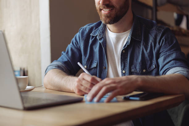 istock Hands of caucasian man with pen while taking notes at laptop at table. Male noting at computer. 1394954793