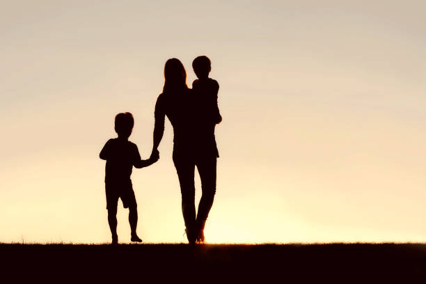 Silhouette of Walking Mother and Young Children Holding Hands at stock photo