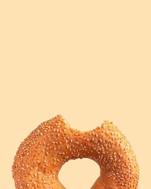 Fresh bitten round wheat bagel with sesame seeds isolated on beige background. Crispy bread, healthy organic food, traditional pastries, bakery product. Breakfast bagel, cut out element for advertising.