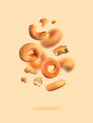 Creative food, baking layout. Fresh round wheat bagel with sesame seeds flying on beige background. Crispy bread, healthy organic food, traditional pastries, bakery product. Breakfast bagel.