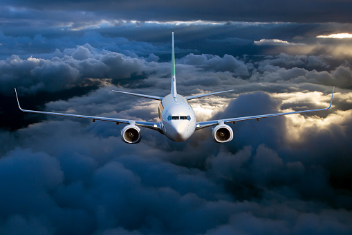 Plane is flying on blue sky at sunset.