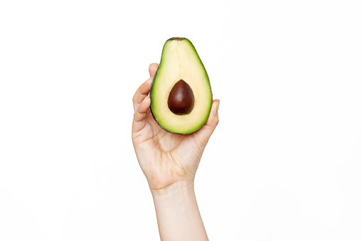 A female hand holding a half an avocado isolated on a white background. Diet, weight loss and wellness, healthy lifestyle. Natural cosmetics