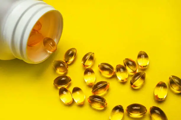 Capsules pill with vitamin D poured out of white plastic packaging on yellow background. Fish oil, Omega, Omega-3, dietary supplement, sunshine vitamin. Healthy lifestyle, medicine, cosmetology, diet.