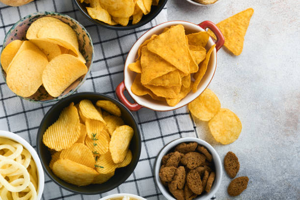 schnellimbisse. ungesundes essen. alle klassischen kartoffelsnacks mit erdnüssen, popcorn- und zwiebelringen und gesalzenen brezeln in schüsseltellern auf grauem betonhintergrund. ungesunde nahrung für figur, herz, haut, zähne - onionskin stock-fotos und bilder