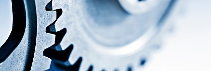 A steel blue cast dominates a close up of two interlocked gears photographed with a very shallow depth of field.