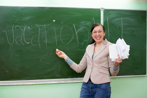 Happy teacher writes the word vacation on the blackboard.