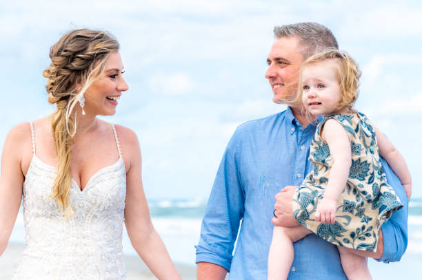 bella sposa tiene un bambino carino su una spiaggia in abito da sposa. piccolo matrimonio di destinazione familiare o fuga d'amore - elope foto e immagini stock