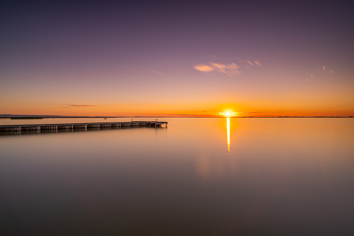 Long exposure shot early in the morning at sunrise on calm lake, sunlight reflecting in water, swimming pier