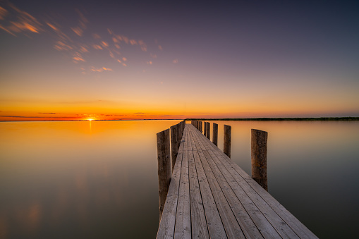 Long exposure shot early in the morning sunrise on calm lake with wooden jetty at good weather in summer season view till the horizon