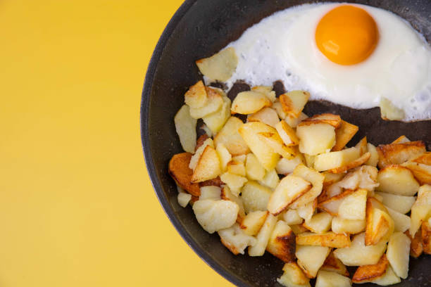On a yellow background frying pan with fried potatoes and scrambled eggs.