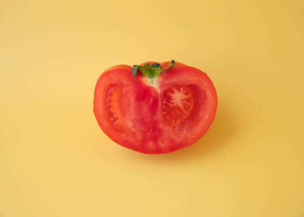 istock On a yellow background, a half of a red tomato with a green tail 1394988423