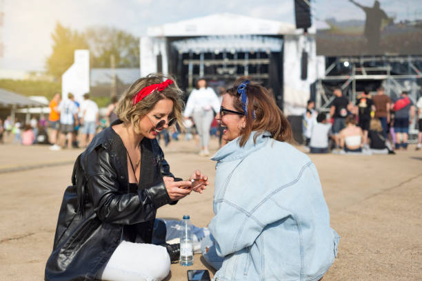 Young female friends having fun and using mobile phone  at a music festival stock photo