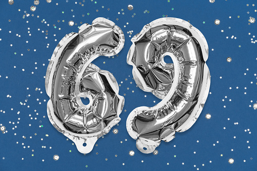 Silver foil balloon number, digit sixty nine on a blue background with sequins. Birthday greeting card with inscription 69. Top view. Numerical digit. Celebration event, template.