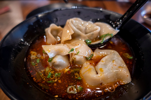 Close up, selective focus on dumplings inside a bowl of hot and sour soup at a Chinese restaurant