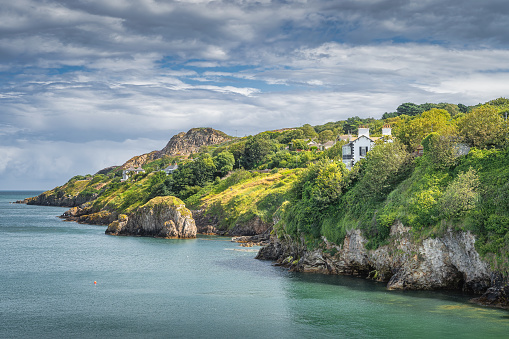 Turquoise coloured Irish Sea, small rocky islands, Howth cliff walk with some residential houses and lush green vegetation, Dublin, Ireland