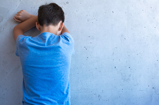 Depressed crying sad boy stand back alone and leaning on the wall. Learning difficulties, family problems, bullying, depression, stress or frustration concept