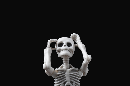 Skeleton figurine hold its head by black background. Desperate figure on dark backdrop. Stressed and sad doll, mental problems, feeling bad, depressed, disappointment, hopeless emotions concept