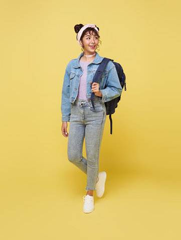 Asian girl students with bags walking towards class college isolated against yellow studio background