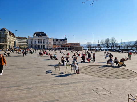 Teh Sechseläuten Platz is a large Square in the City of Zurich. The image was captured during spwing season with several people sitting on chairs and relaxing.