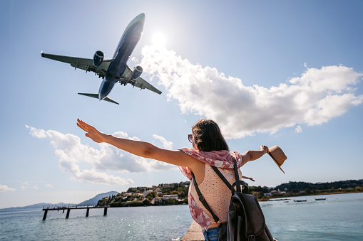 Beautiful young female tourist spreading her arms as the airplane flies above her in Corfu Town, Greece.