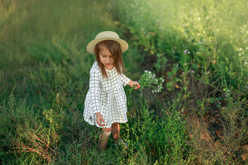 Beach portrait of a beautiful little girl aged 8 smiling at the camera. The girl is wearing a straw cowboy hat and a sundress. Sunny summer day.