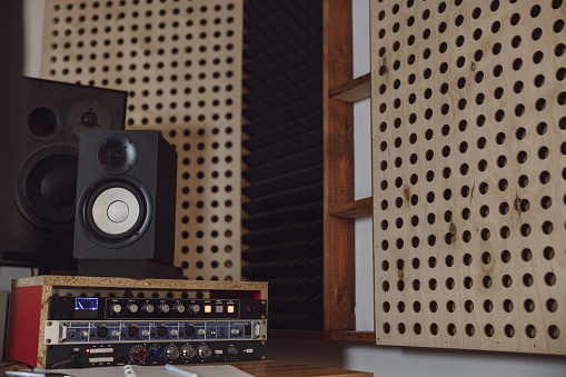 Musical sound speakers near soundproof room with wooden wall with round holes and black soundproof wall with acoustic dampening foam in a professional sound recording studio