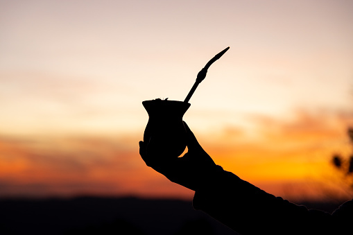 Silhouette of a hand holding a yerba mate gourd drink at sunset