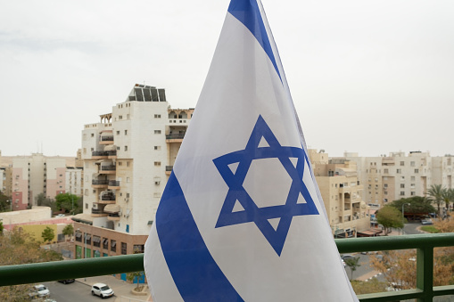 Flag of state Israel on the occasion of Independence day  (Yom Haatzmaut) in israel. Typical israeli architecture in the background. Israeli Star of David official flags.